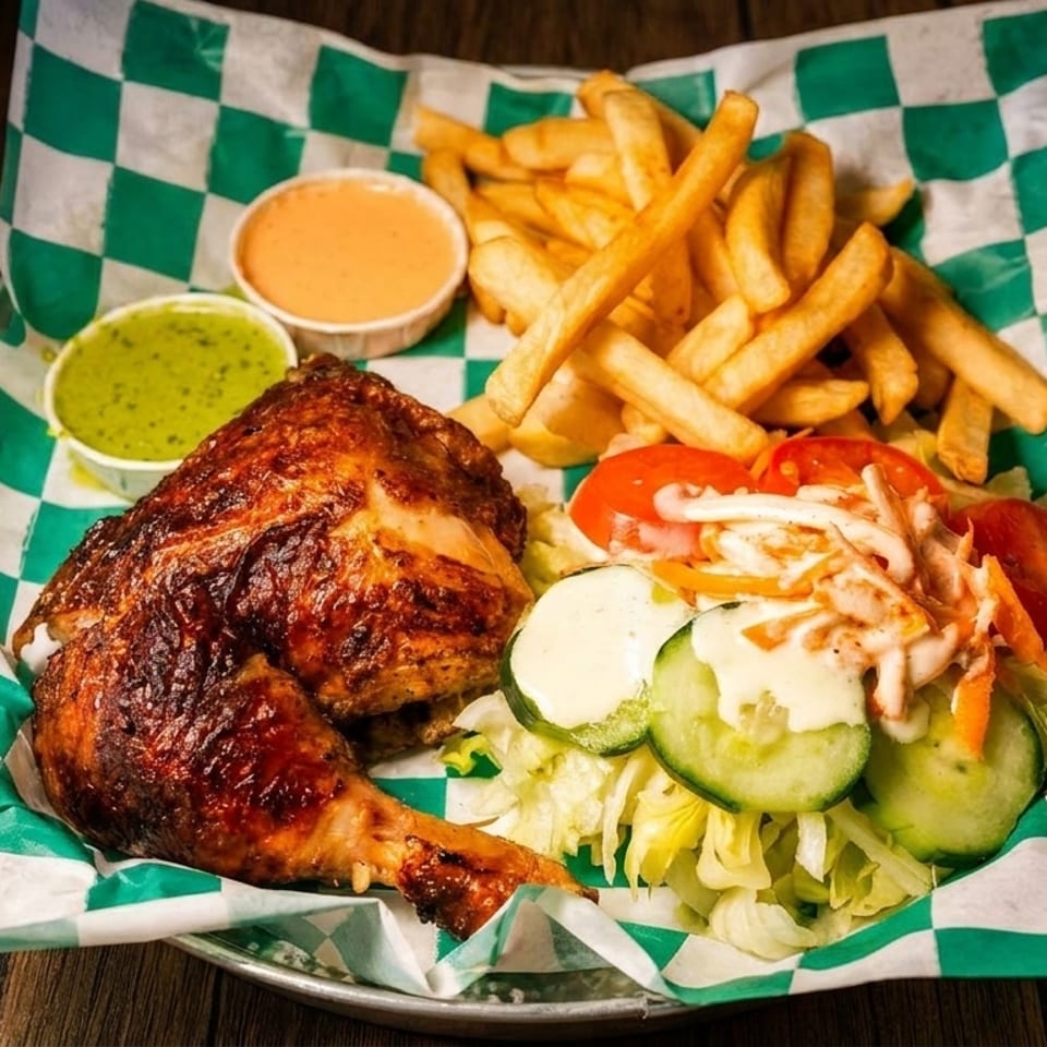 Grilled chicken leg and thigh with fries, salad, and two dipping sauces on checkered paper.